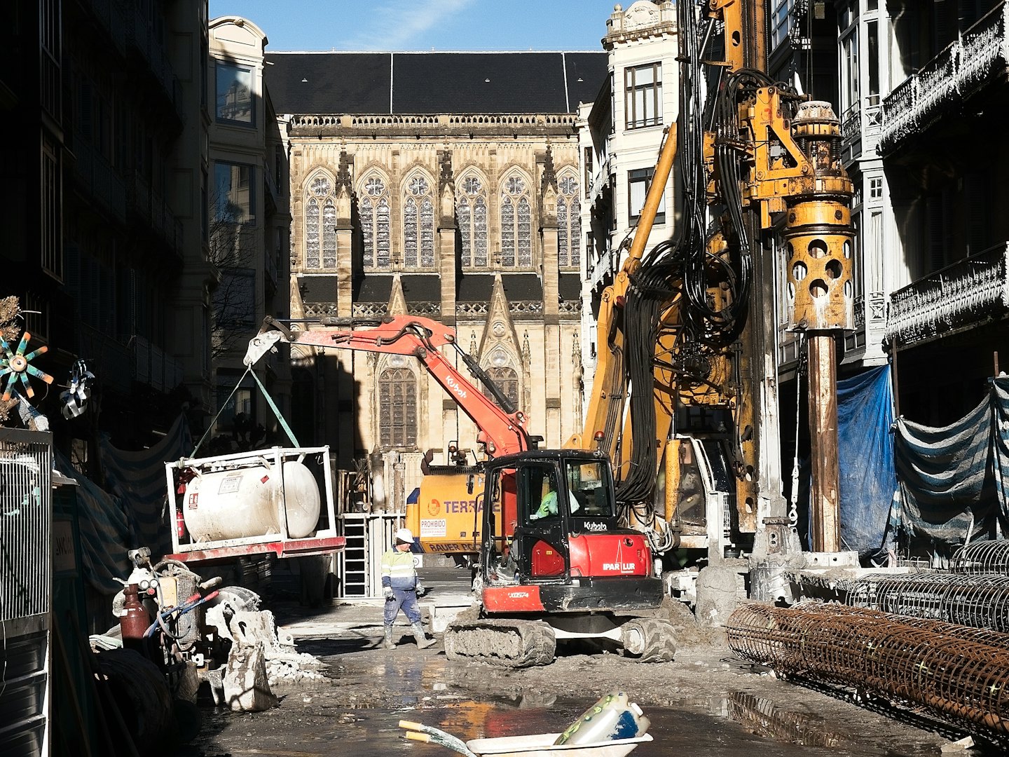 Home Operaio edile supervisiona macchinari pesanti in un cantiere urbano fangoso.
